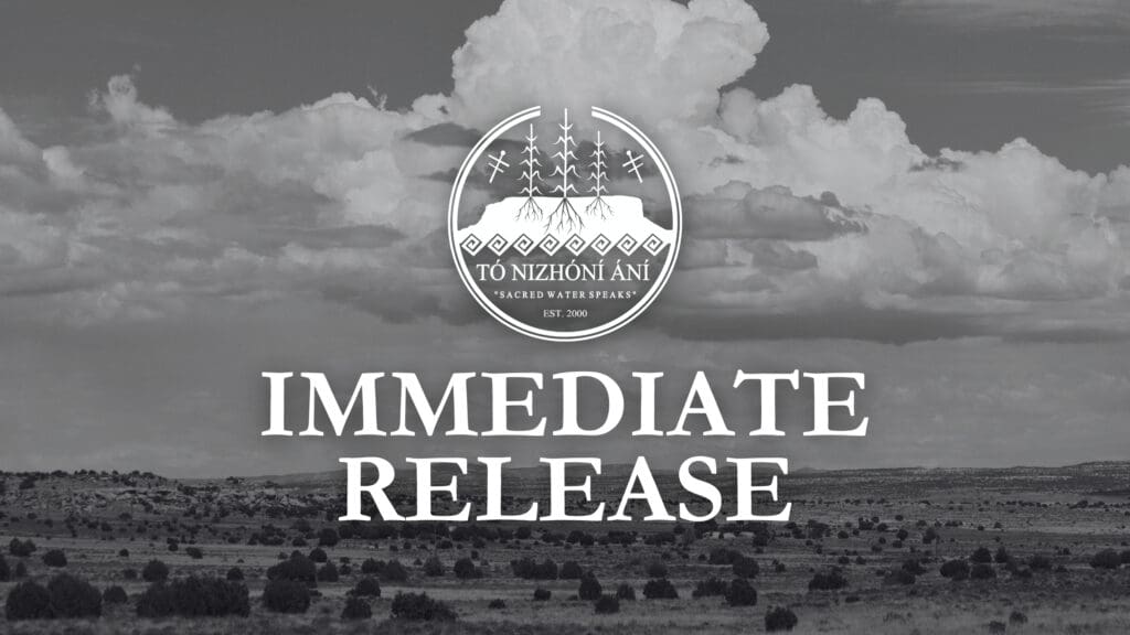 Black and white image of a landscape with expansive clouds over a flat terrain, featuring a central logo that reads "tó nizhóní ání, sacred water speaks, est. 2001" with the words "immediate release" below.