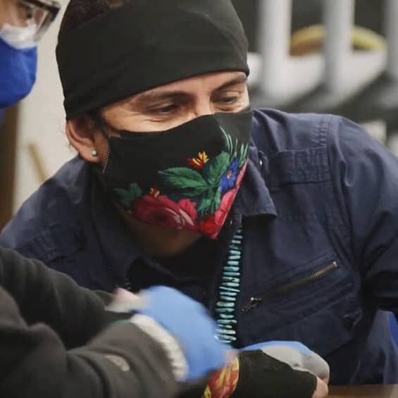 A man wearing a face mask is working on a tattoo.