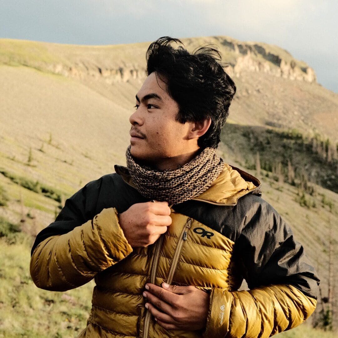 A man in a yellow jacket standing in the mountains.